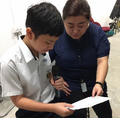 Miss Cao Yu, guiding a Secondary 2 student in delivering The Daily News @ AES